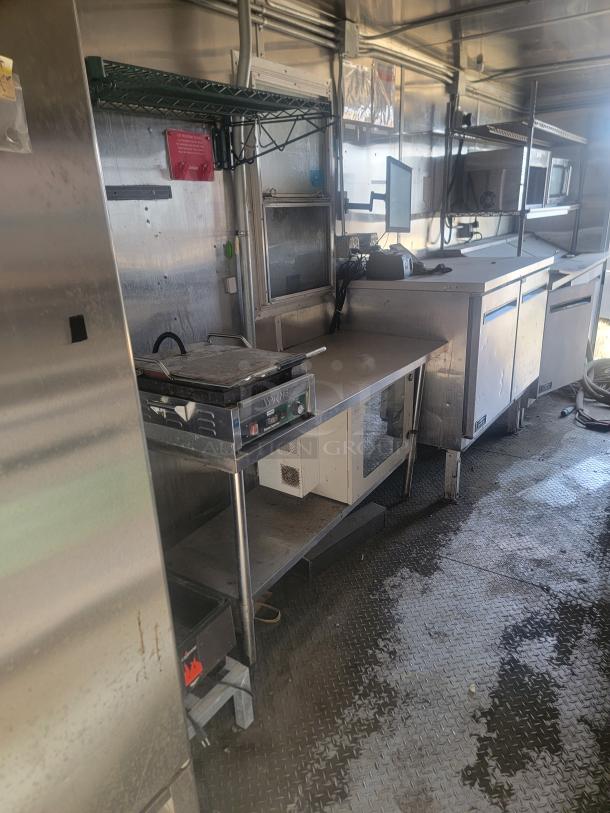 Commercial kitchen setup with stainless steel countertops, industrial appliances, and storage shelving in used condition.