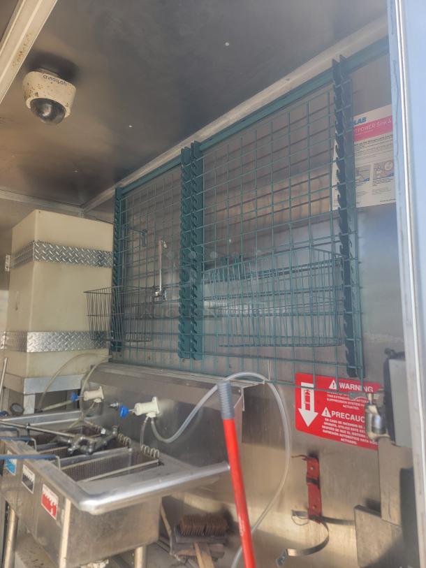 Commercial food truck interior featuring dual sink setup, water hoses, wire racks, and warning labels. Clean and functional condition.