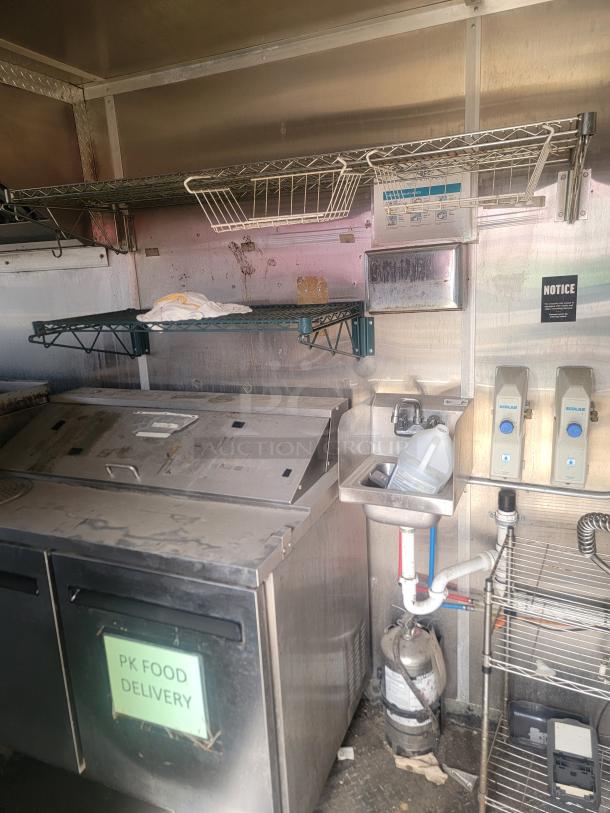 Commercial stainless steel food delivery station with shelves, sink, and fire extinguisher; includes Ecolab dispensers and PK Food Delivery label.