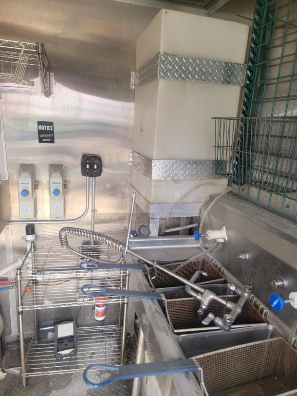 Commercial deep fryer setup with multiple fry baskets, stainless steel shelving, and wall-mounted cleaning solution dispensers.