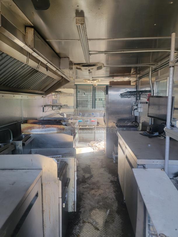 Commercial kitchen interior with stainless steel appliances, ventilation hood, shelving, and equipment. Worn condition, some rust visible.