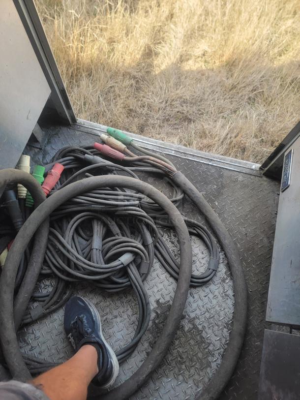 Coiled cables with colored connectors on metal flooring, showing signs of wear. Outdoor setting with dry grass visible.