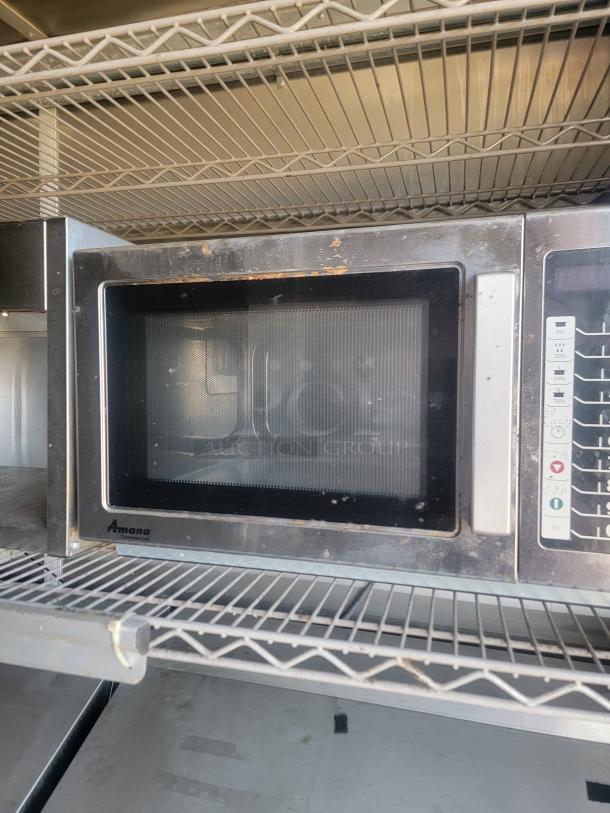 Amana commercial microwave with visible wear on stainless steel finish, digital control panel, and standard wire shelf placement.