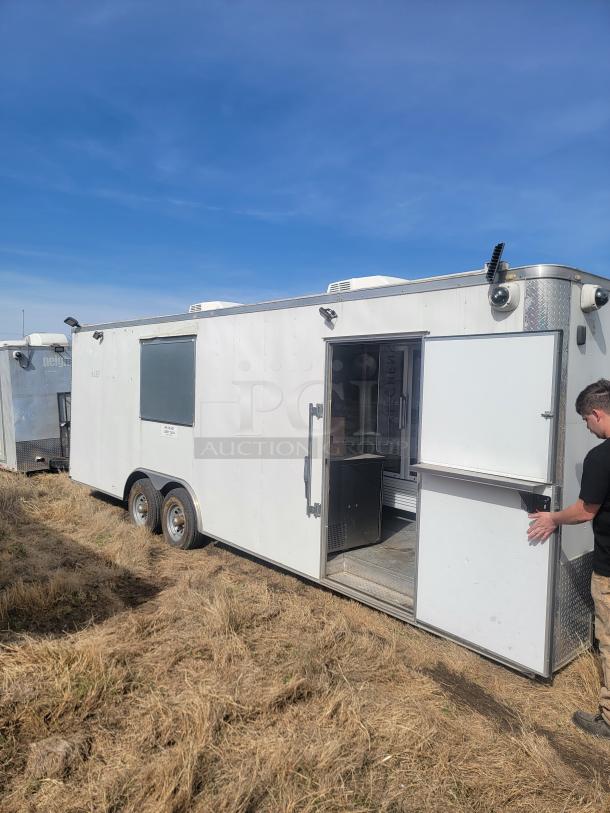 White enclosed trailer with double axles, side window, and exterior door open. Moderate wear, parked on dry grass.