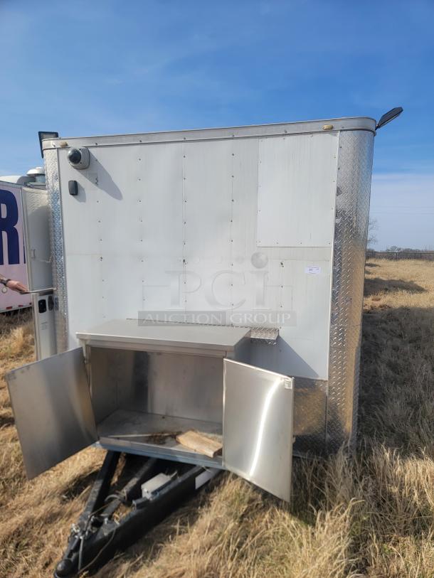 Enclosed utility trailer with diamond plate trim, open front compartment, and visible wear. Ideal for storage or transport.