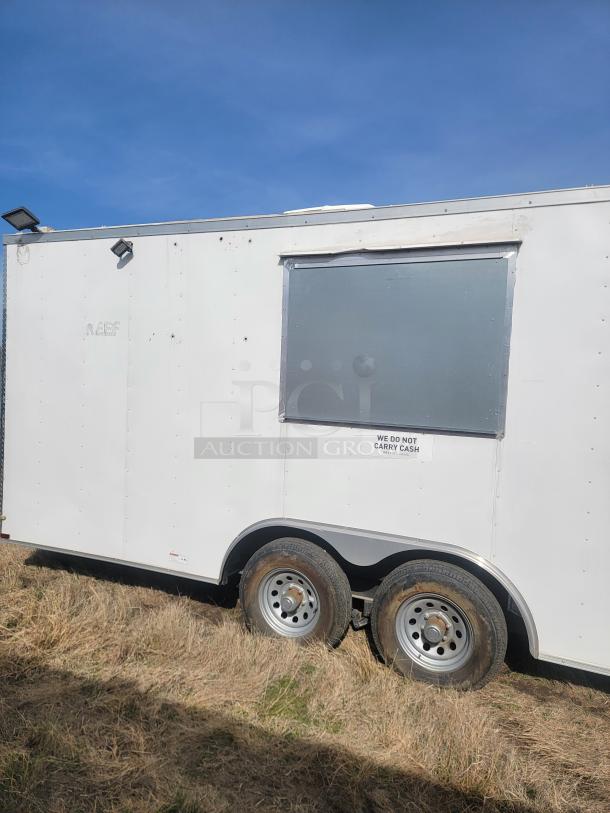 White enclosed trailer with dual axles, outside serving window, "We do not carry cash" sign, and custom lighting.
