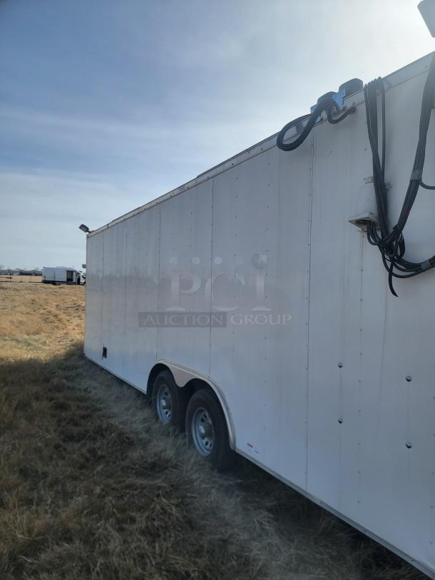 White enclosed utility trailer with dual axles, parked on grass. Features exterior wiring on the side. Good condition.