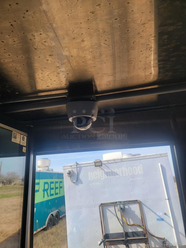 Ceiling-mounted security camera with a glass dome, installed in an industrial setting. View of trailers outside.