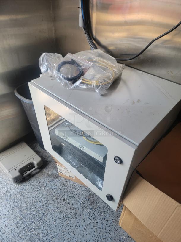 Metal cabinet with a glass door, used for networking equipment. Includes packaged cables. Moderate wear visible on surface.