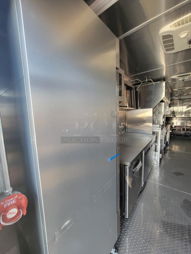 Commercial kitchen interior featuring stainless steel appliances, including a large fridge, counters, and ventilation.