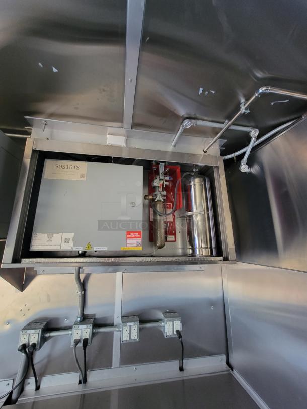 Commercial kitchen fire suppression system with control panel, red and silver components, visible piping, and electrical outlets.