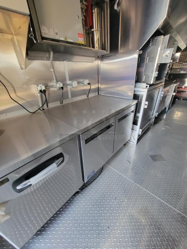 Stainless steel commercial kitchen setup with under-counter refrigerator, pristine condition, power outlets above.