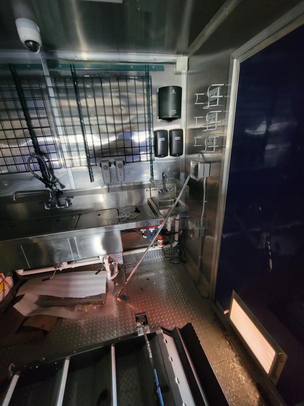 Stainless steel mobile kitchen interior with sink, storage racks, soap dispensers, and visible plumbing. Clean, good condition.