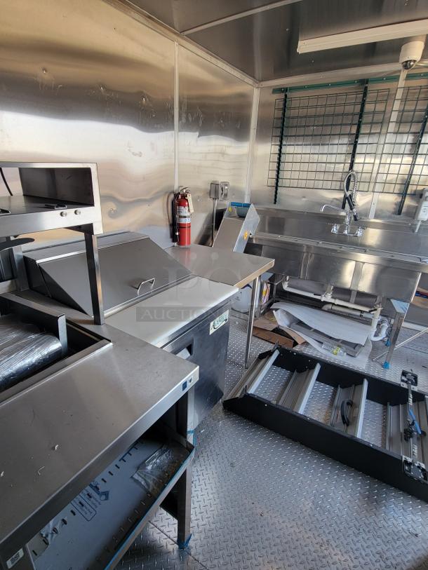 Commercial kitchen interior with stainless steel surfaces, double sink, and equipment. Includes fire extinguisher and storage spaces.