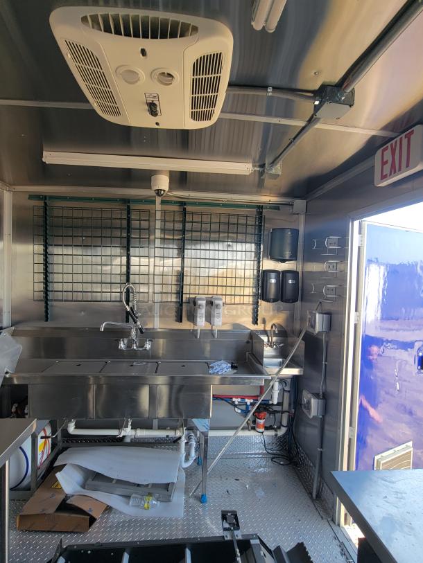 Mobile kitchen interior with stainless steel sink, ventilation system, and storage. Equipped with soap dispensers and exit sign.