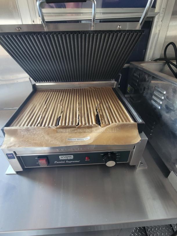 Waring Commercial Panini Supremo grill, open, with corrugated paper. Features on/off switch, heat dial, and "Remove Before Use" label.