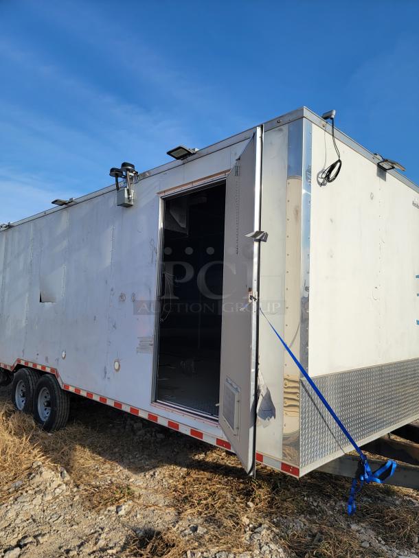 Enclosed utility trailer with dual axles, open door, and exterior lights. Some wear visible on metal paneling. Suitable for transport or storage.
