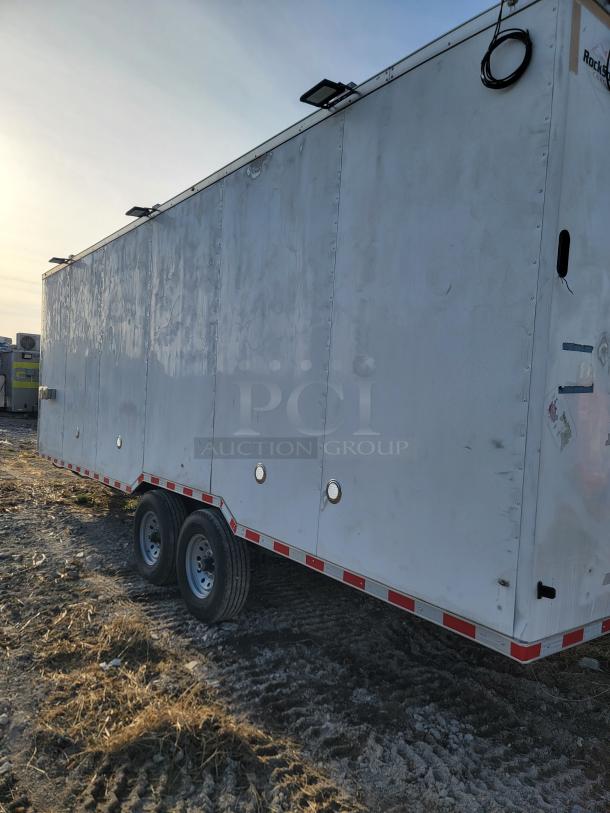 Large white utility trailer with dual axles and exterior lighting. Visible wear with a company logo on the side.