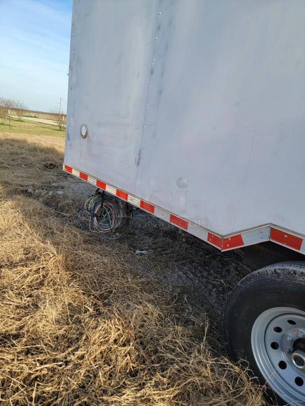 Large white trailer on grass, featuring red reflective stripes and visible wheel. Wiring exposed at base, condition appears used.