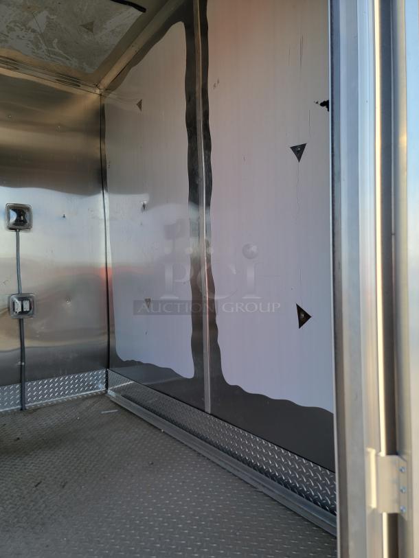 Interior of a metal trailer showing diamond plate flooring, wall outlets, and some surface dents. Interior appears used.