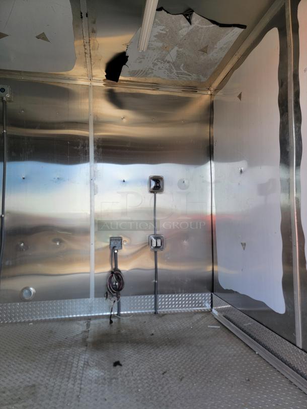 Interior of metal storage unit with visible wiring and damaged ceiling. Diamond plate flooring, some wear and tear.