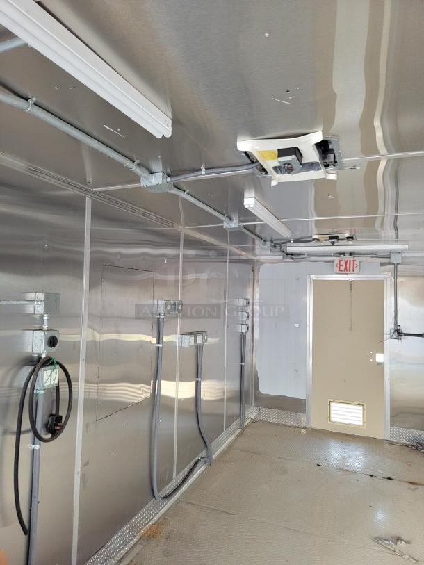Industrial trailer interior with metallic walls, overhead lighting fixtures, electrical outlets, and an exit sign. Clean condition.