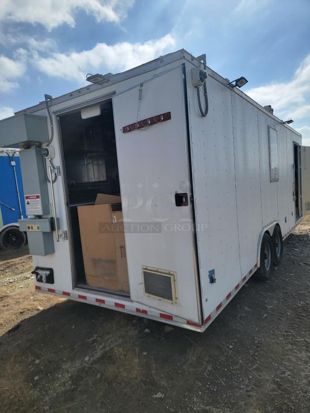 Mobile trailer with open door, dual axles, and utility panel. Some exterior wear visible. Equipped with hooks and vents.