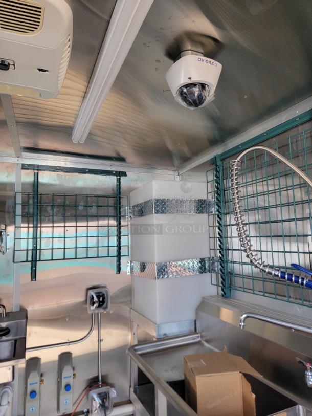 Industrial kitchen interior with stainless steel surfaces, Avigilon security camera, sinks, and storage racks. New condition.