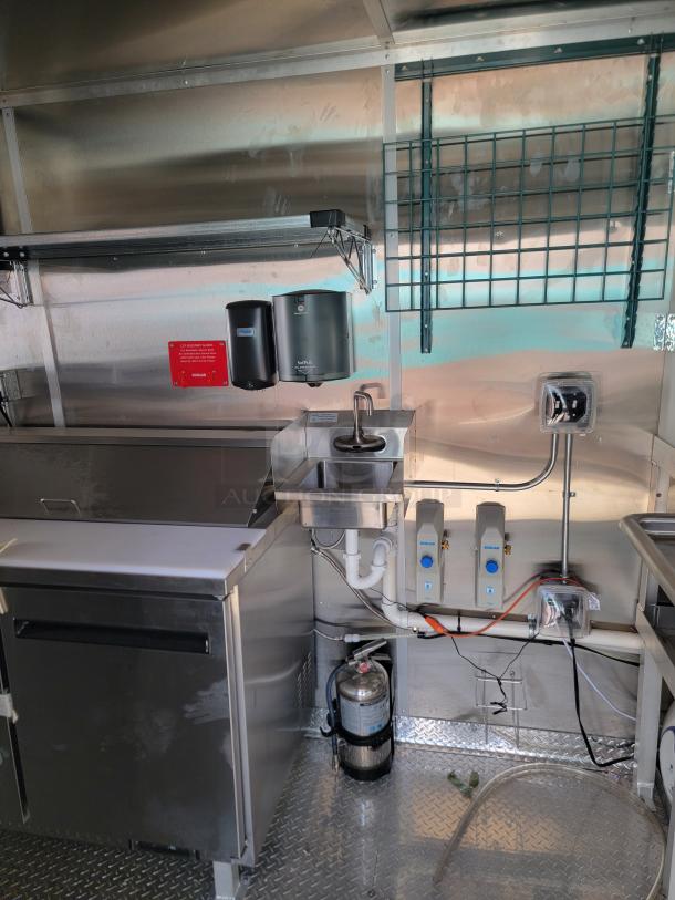 Commercial kitchen setup featuring stainless steel surfaces, a small sink, paper towel dispensers, and a fire extinguisher in great condition.