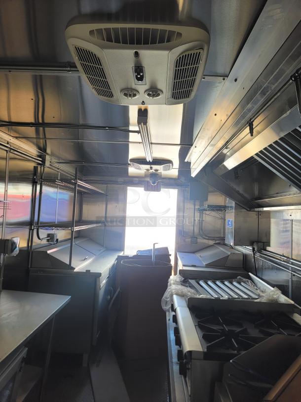Interior of a mobile kitchen trailer with stainless steel appliances, industrial ventilation, stovetop, and prep areas. Good condition.