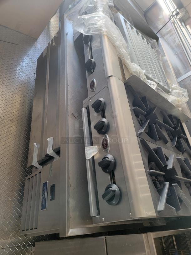 Stainless steel commercial kitchen stove with grill, brand "Wells." Features multiple burners, control knobs, excellent condition.