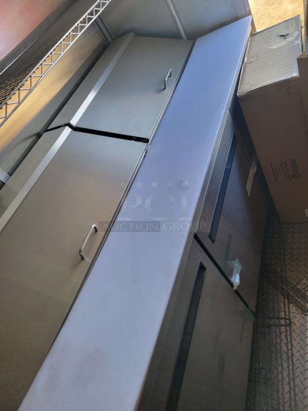 Stainless steel commercial refrigerator, double door, metallic finish, with sturdy handles and visible shelving unit above.