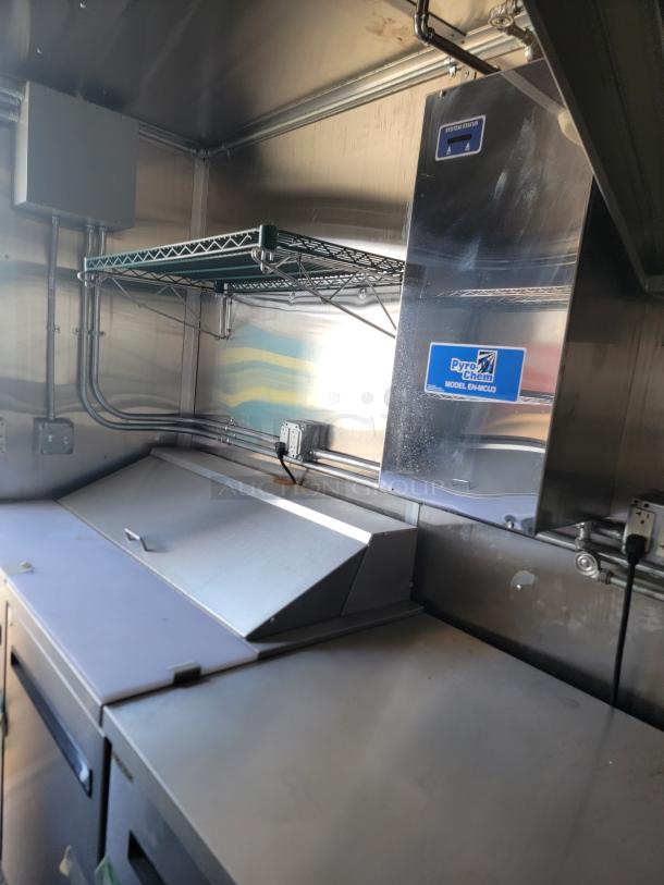 Commercial kitchen setup with Pyro-Chem EM-MCU3 system. Stainless steel surfaces; overhead wire shelving. Good condition.