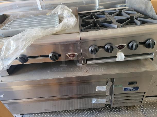 Wells stainless steel commercial stovetop with griddle and 4-burner range, attached to Arctic Air refrigerator. Appears in good condition.