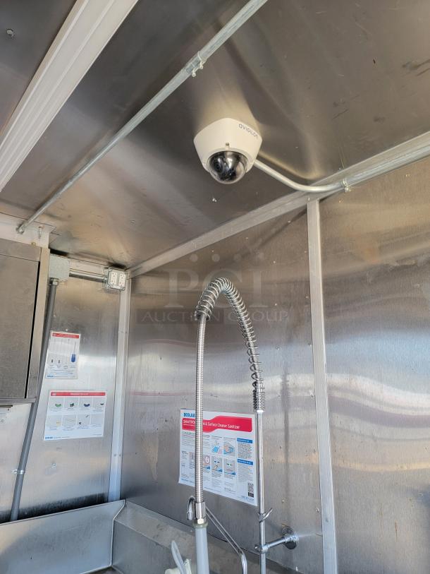 Avigilon CCTV dome camera installed on a metallic ceiling, next to a commercial sink with cleaning instructions on the wall.