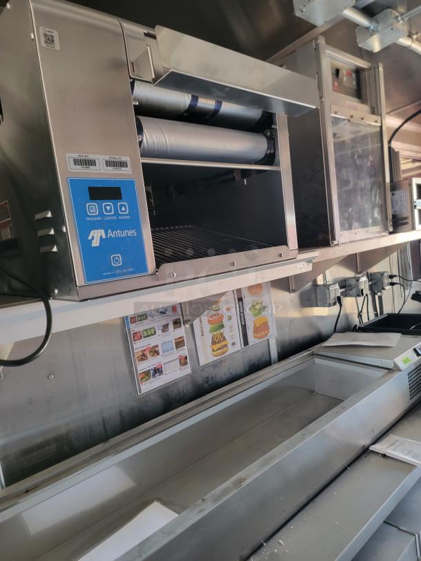 Alt text: Antunes commercial kitchen toaster with digital controls, open chamber, and metal rollers. Visible labels show model details.