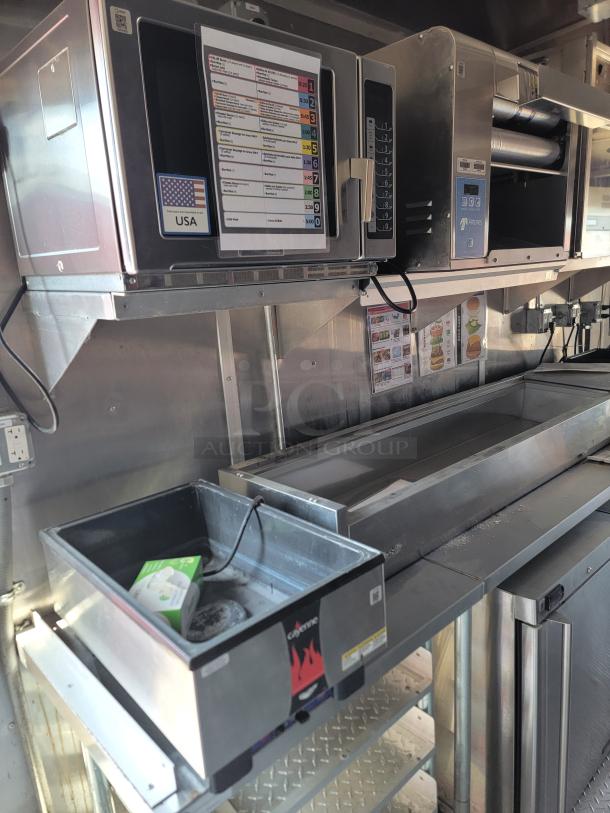 Commercial kitchen equipment including a USA-made microwave, conveyor oven, and warming drawer. Features include control panels and heating elements, suitable for food service use.