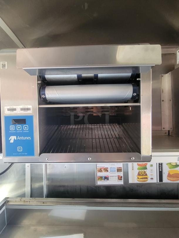 Antunes commercial toaster, stainless steel, dual rollers, control panel on side, visible info tag and instruction labels.