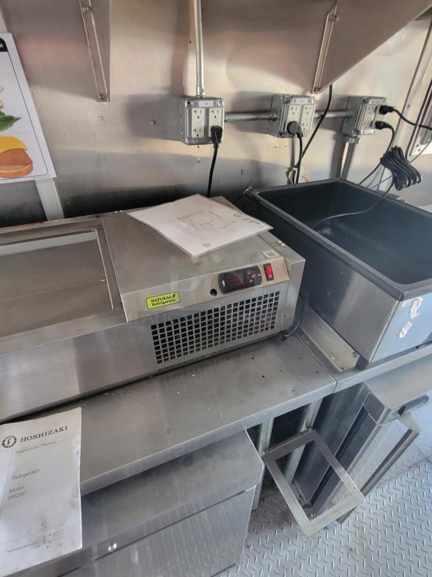 Hoshizaki HR24C refrigerator on a metal counter, with instruction manual and visible "Natural Refrigerant" label.