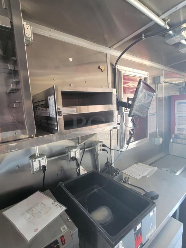 Commercial stainless steel kitchen setup with mounted microwave, electrical outlets, and storage bins in used condition.