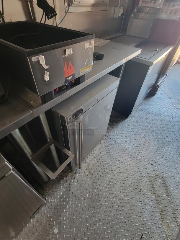 Commercial kitchen equipment, including a Cayenne food warmer and stainless steel counters, in used condition. Visible wear.