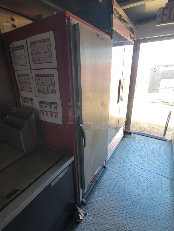Commercial refrigerator with two doors, visible signage, and instructions inside a facility. Medium wear, sturdy condition.