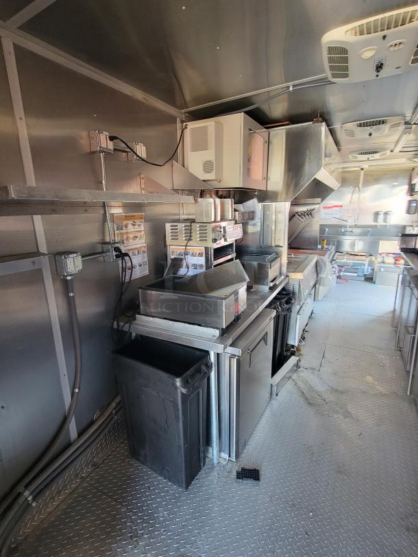 Commercial kitchen trailer interior with stainless steel appliances, overhead ventilation, and electrical outlets. Clean condition.