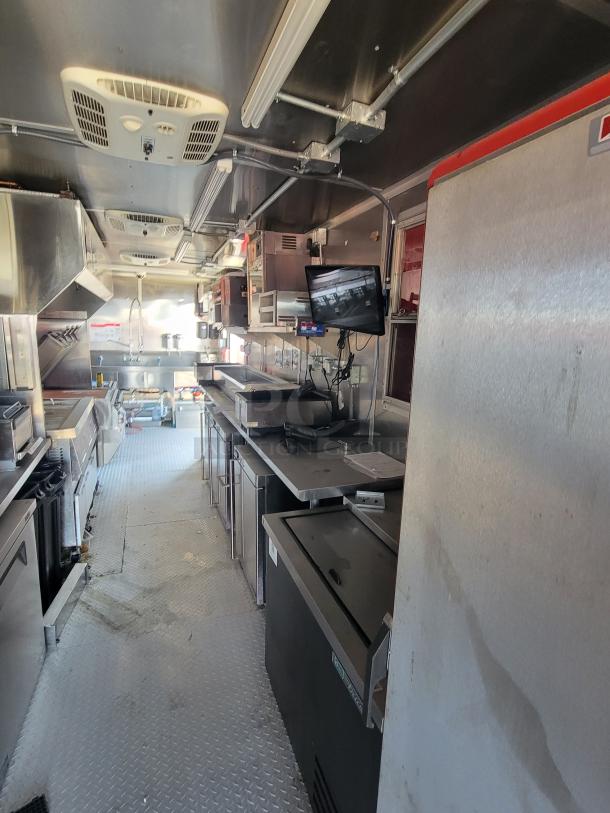 Interior of a commercial kitchen trailer with stainless steel appliances, ventilation, monitors, and diamond plate flooring.
