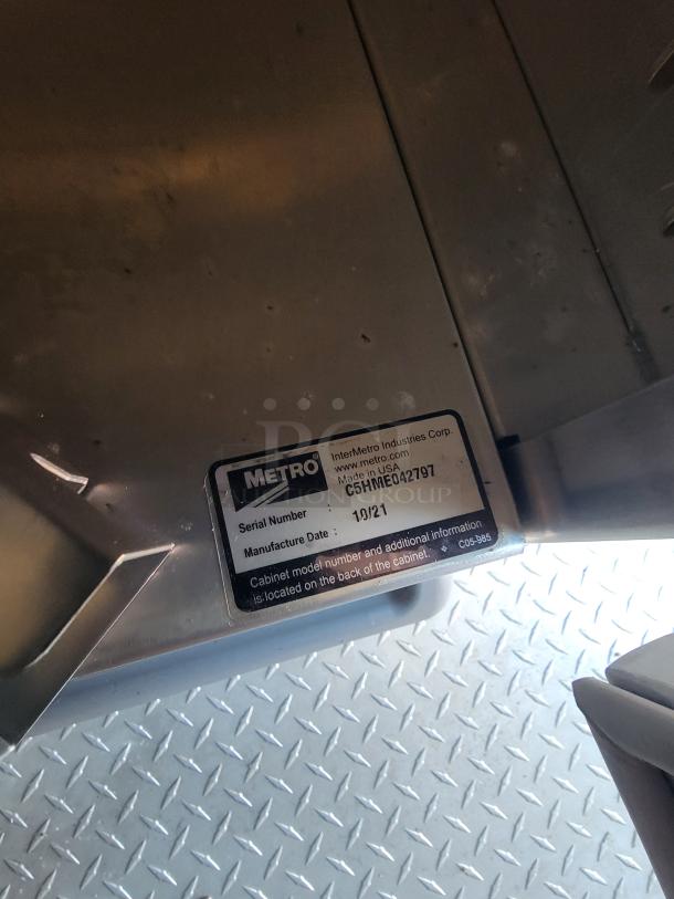 Metal cabinet with Metro label, serial number C5HME042197, manufactured 10/21. View shows label on metal surface.