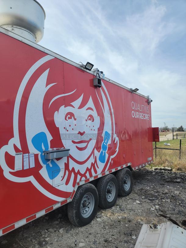 Red food truck with branded graphics and slogan, featuring stainless steel ventilation. Tri-axle, park setting, good condition.