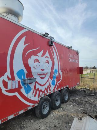 Red food truck with branded graphics and slogan, featuring stainless steel ventilation. Tri-axle, park setting, good condition.