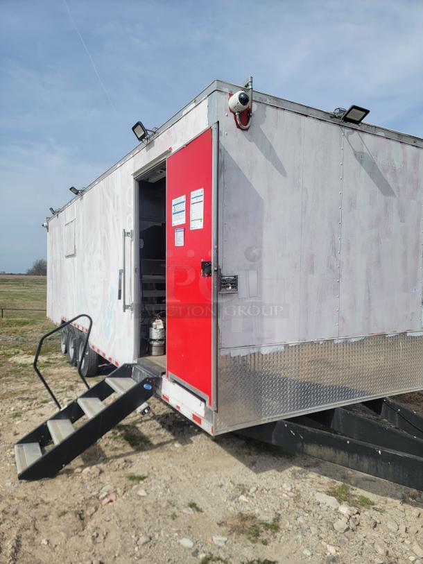 Mobile command trailer with a red door, external security camera, floodlights, and stairs. Signs on door; partially repainted.