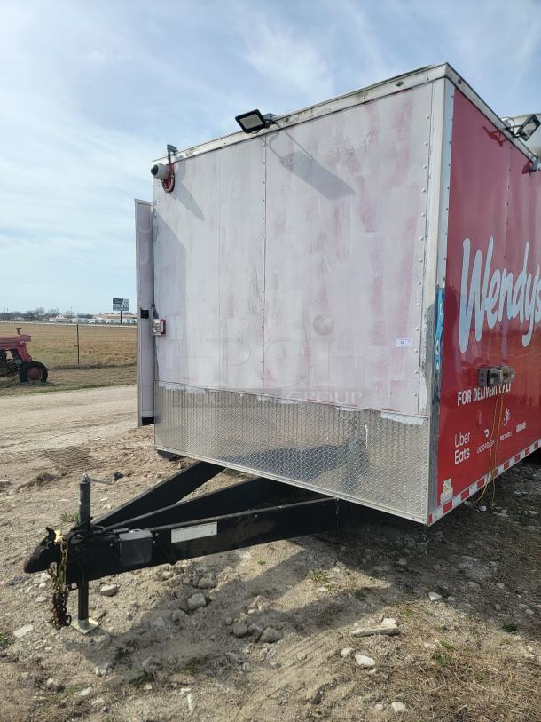 Food trailer with faded Wendy's branding, metal frame, hitch, mounted security camera, and delivery logos. Moderate wear.
