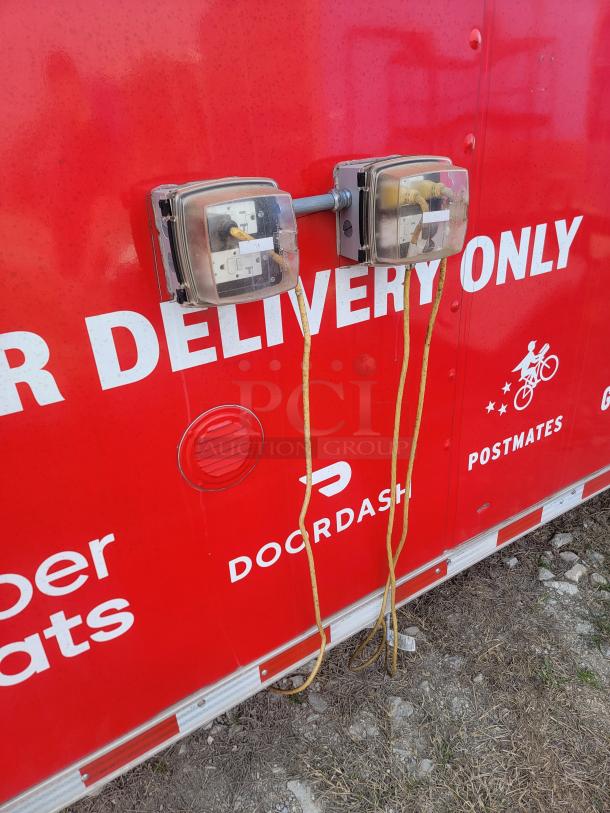 Electrical outlets mounted on a red delivery truck wall, featuring protective covers and yellow cords. DoorDash and Postmates logos visible.